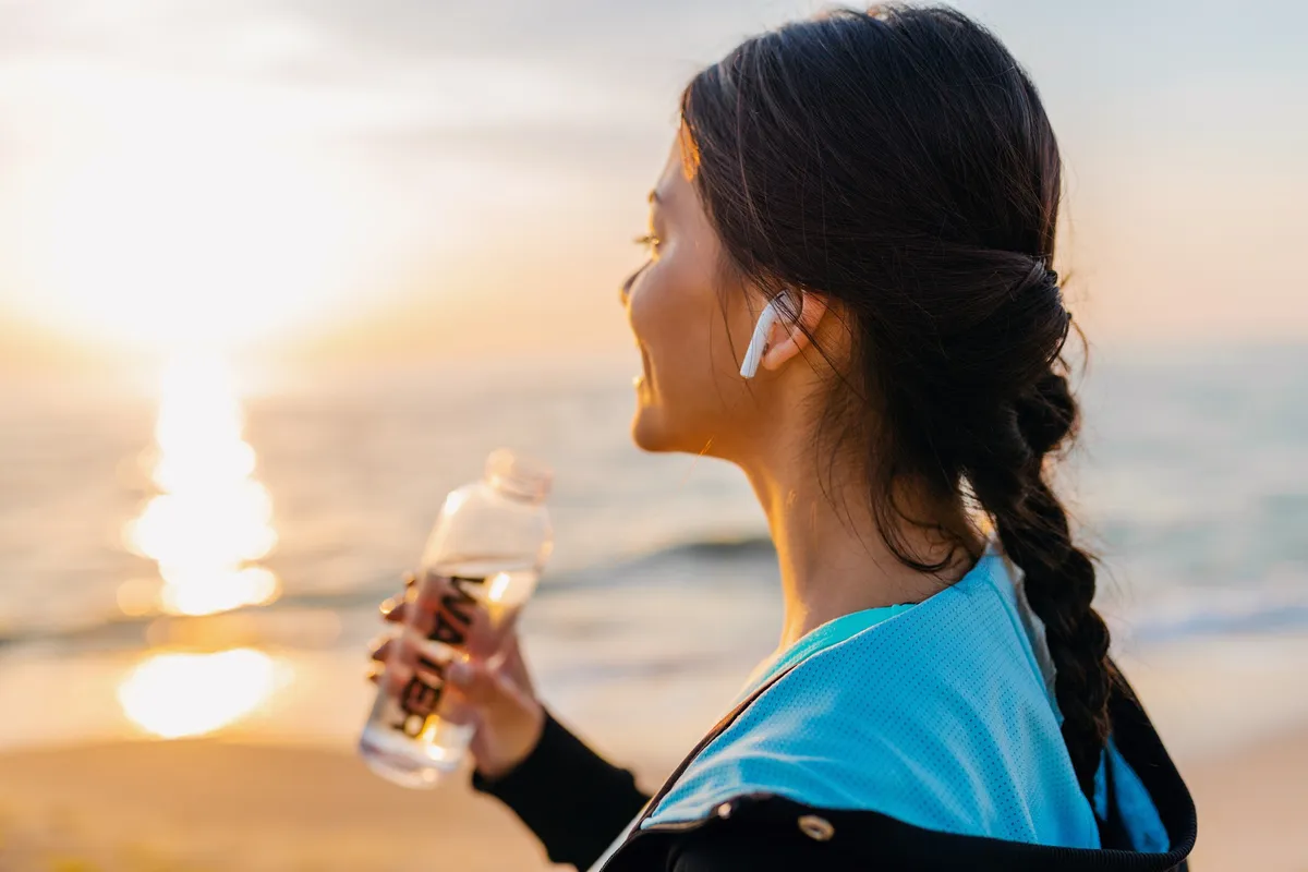 Woman drinking from a water bottle by the sea at sunrise