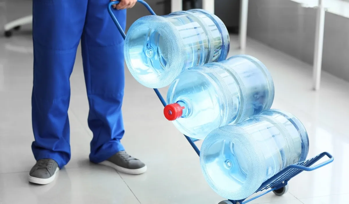 Delivery worker wheeling three 20 litre water jars on a hand trolley