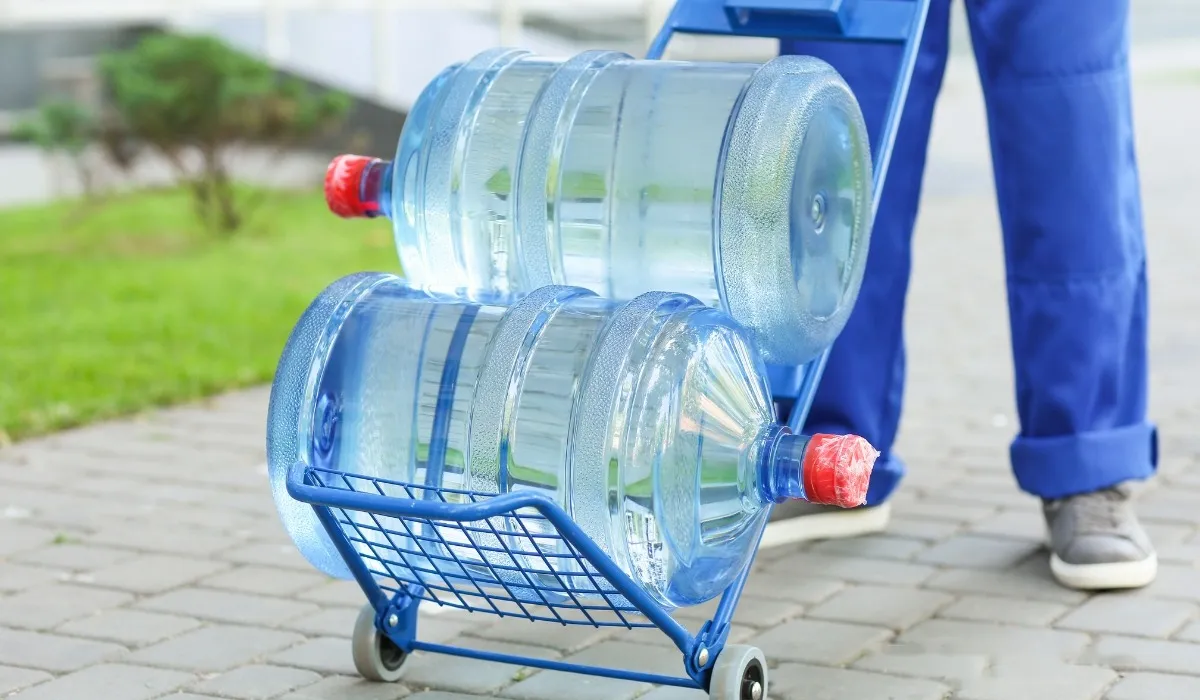 Delivery worker moving two 20 litre water jars on a trolley along a paved path